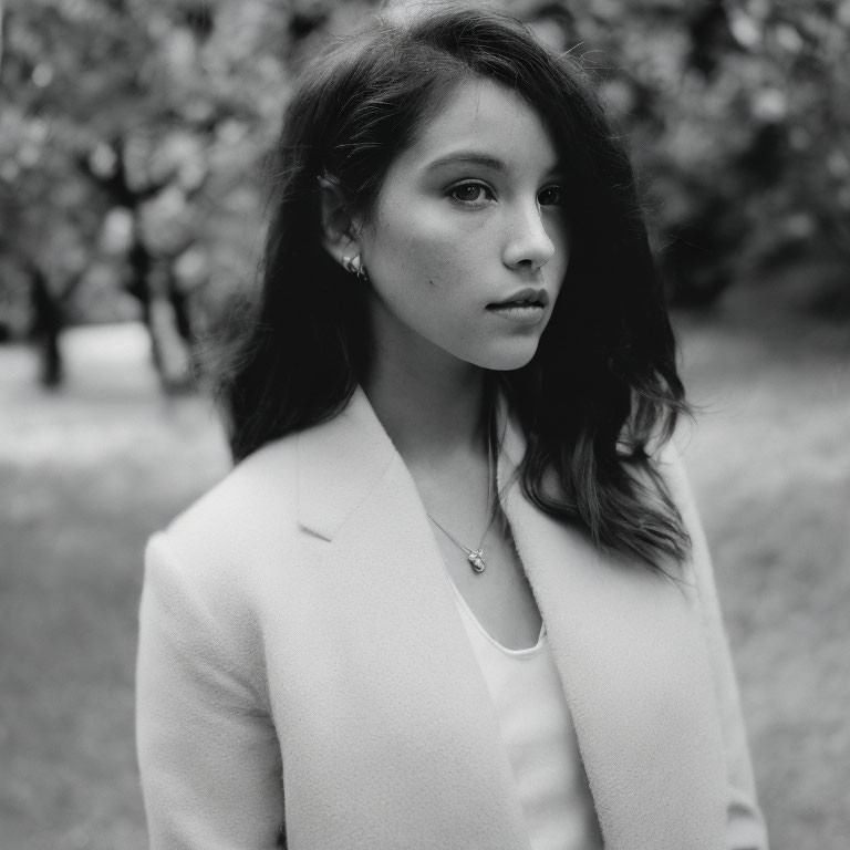 Monochrome portrait of young woman in light coat with blurred trees