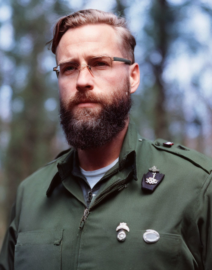 Bearded man in green uniform with badges and glasses in forest setting