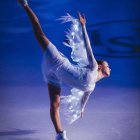 Elegant figure skater in white costume with light-up wings on ice