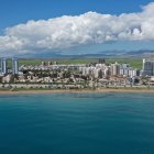 Modern cityscape with bay, beaches, skyscrapers, marina, and mountains under clear sky