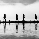 Four silhouetted figures in hats and coats walking in line against urban skyline with reflections.