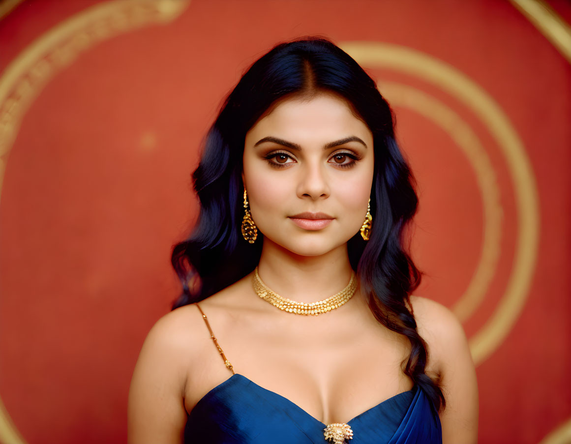 Dark-haired woman in gold jewelry and blue dress against red patterned backdrop