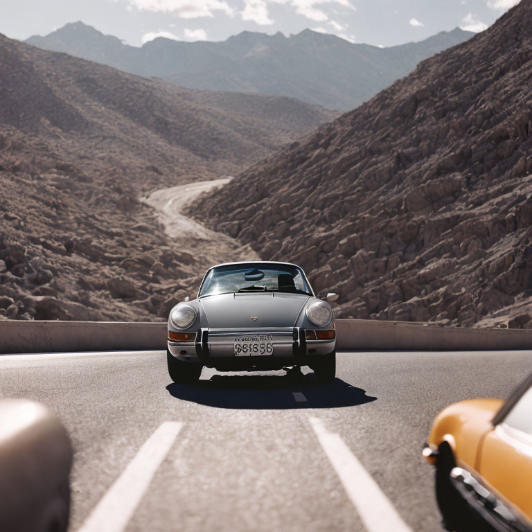 Classic Cars Driving on Mountain Road with Clear Skies & Rugged Terrain