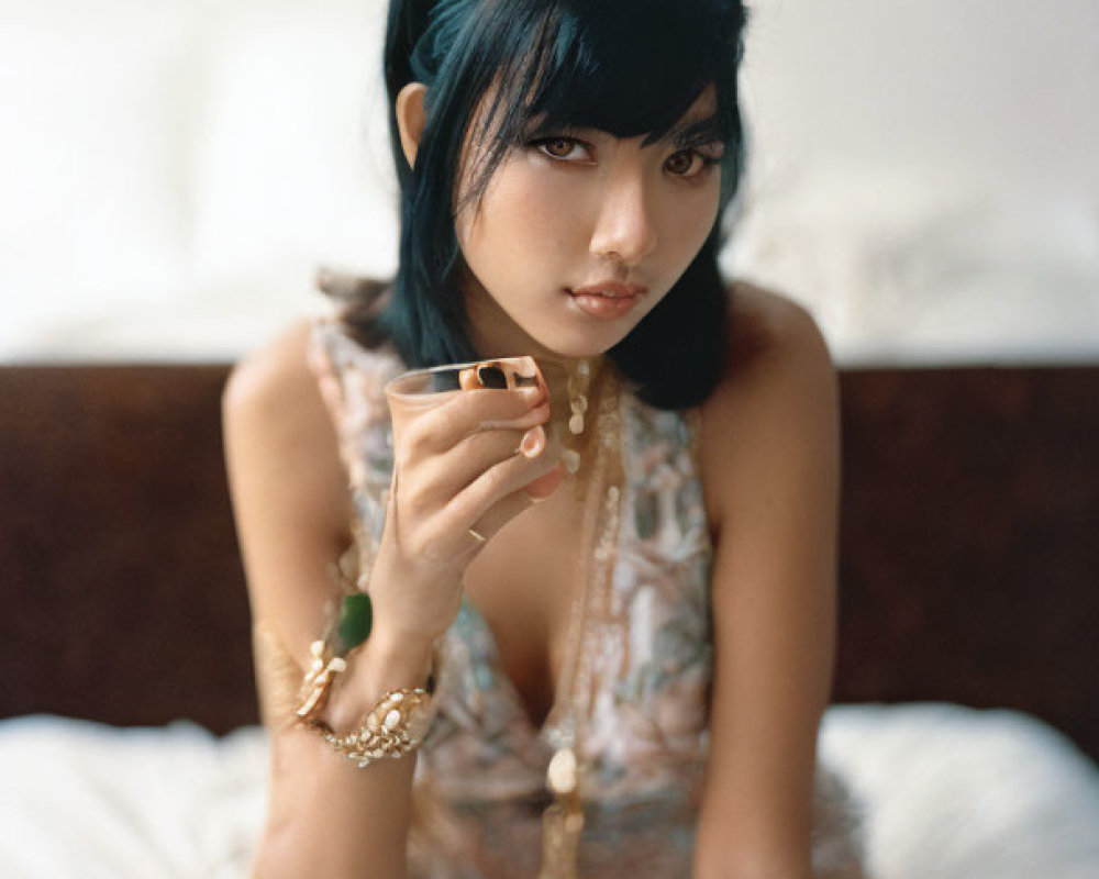 Dark-haired woman in green headband with teacup and jewelry in relaxed pose