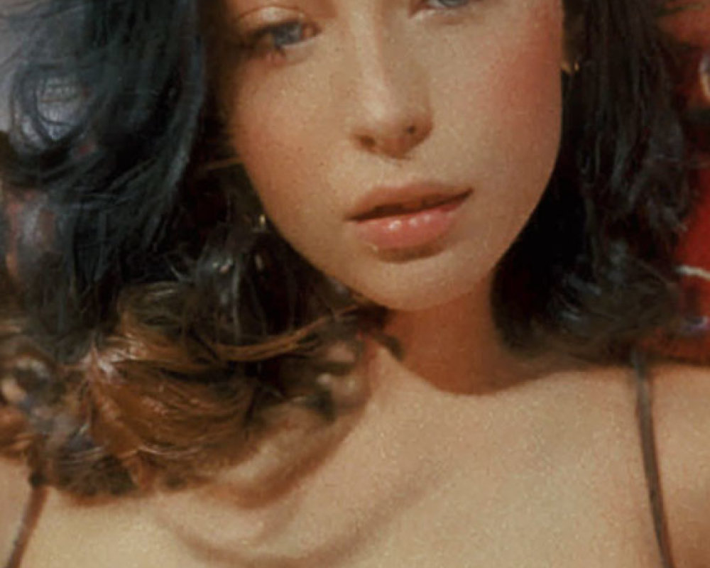 Portrait of woman with wavy brown hair and subtle makeup in black top on red backdrop