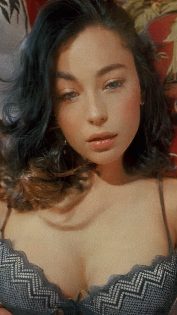 Portrait of woman with wavy brown hair and subtle makeup in black top on red backdrop