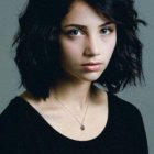 Portrait of young woman with curly black hair and hazel eyes in dark sweater