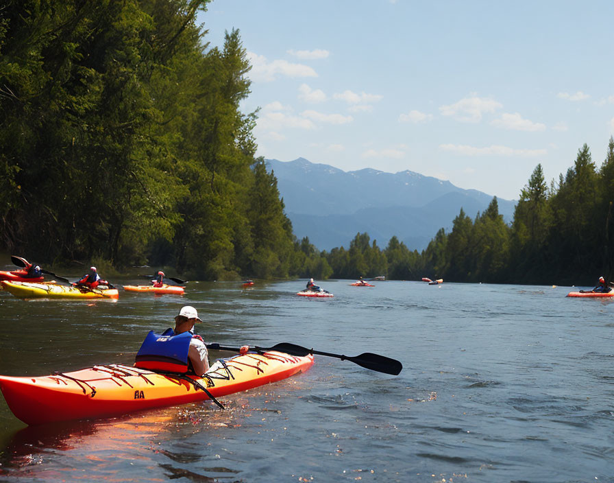 Kayakers on serene river with trees, mountains, and clear sky