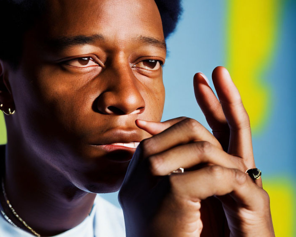 Contemplative individual with afro hairstyle and jewelry against blue and yellow backdrop