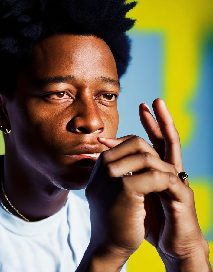 Contemplative individual with afro hairstyle and jewelry against blue and yellow backdrop