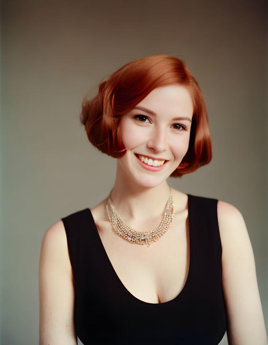 Smiling woman with short auburn hair in black top and pearl necklace