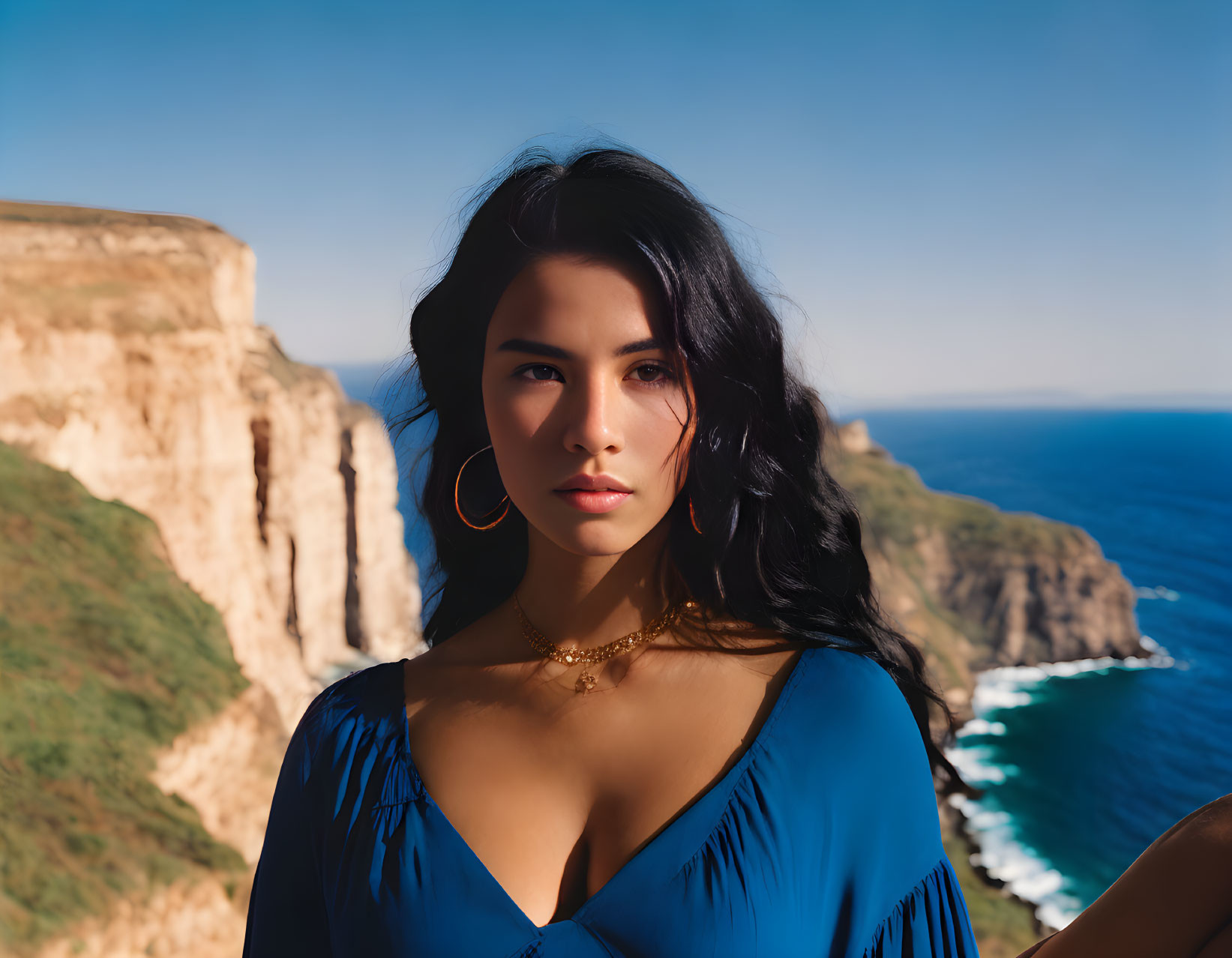 Dark-haired woman in blue top by scenic coast and cliffs.