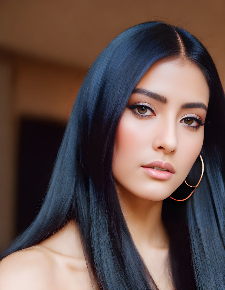 Blue-haired woman with dramatic makeup and gold earrings on blurry background