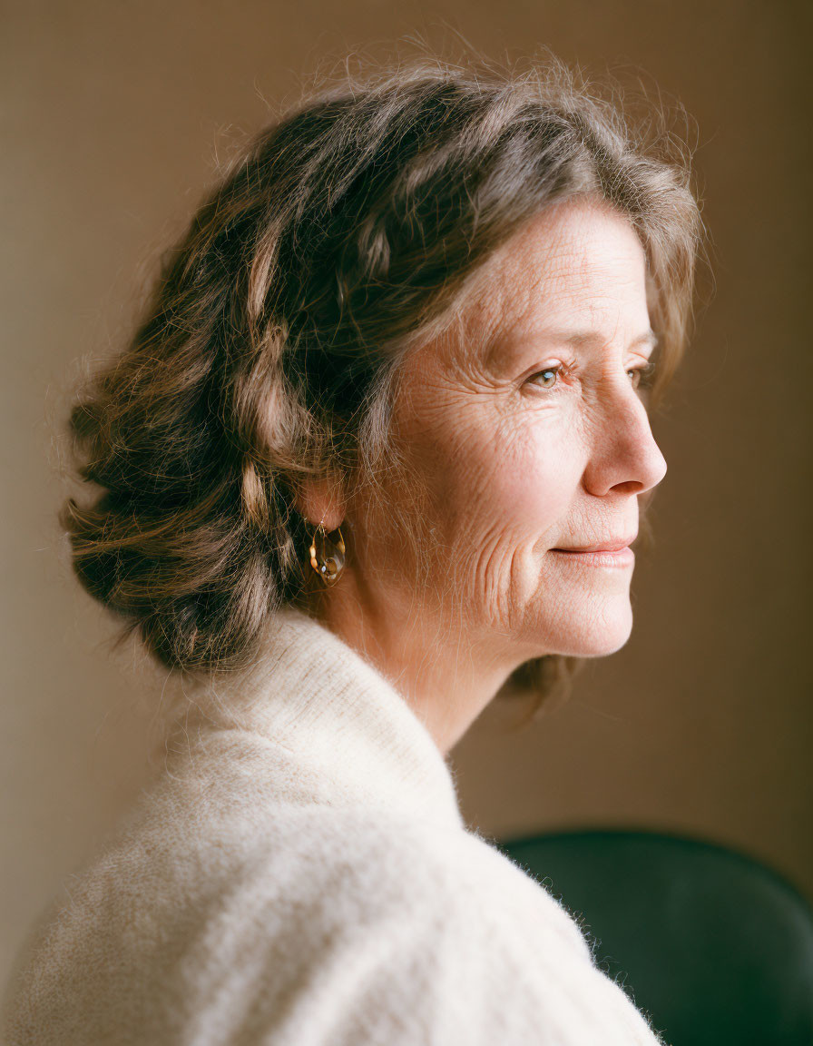 Elderly woman in white sweater gazes contemplatively on beige background