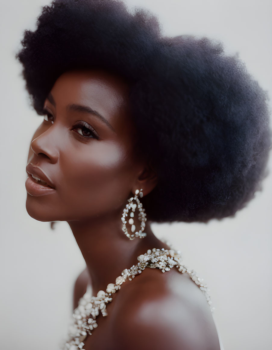 Woman with afro hairstyle and large earrings in bejeweled top gazes away.