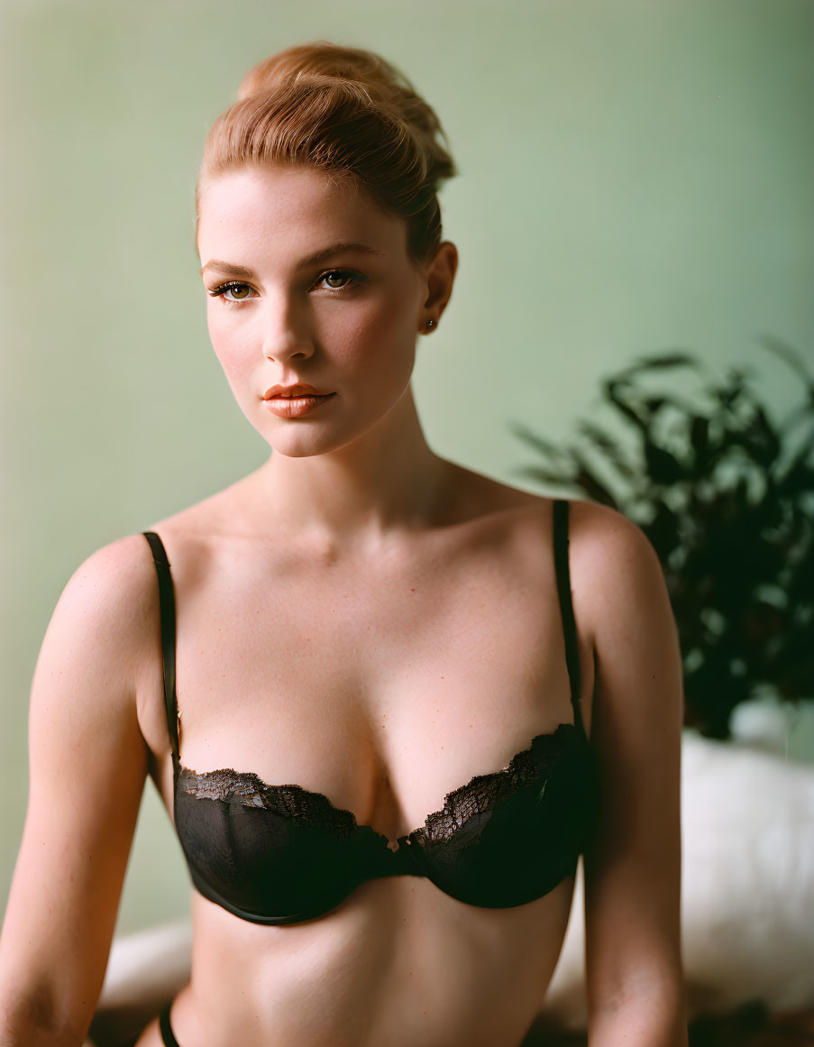 Woman in black lace bra with tied-up hair against green backdrop