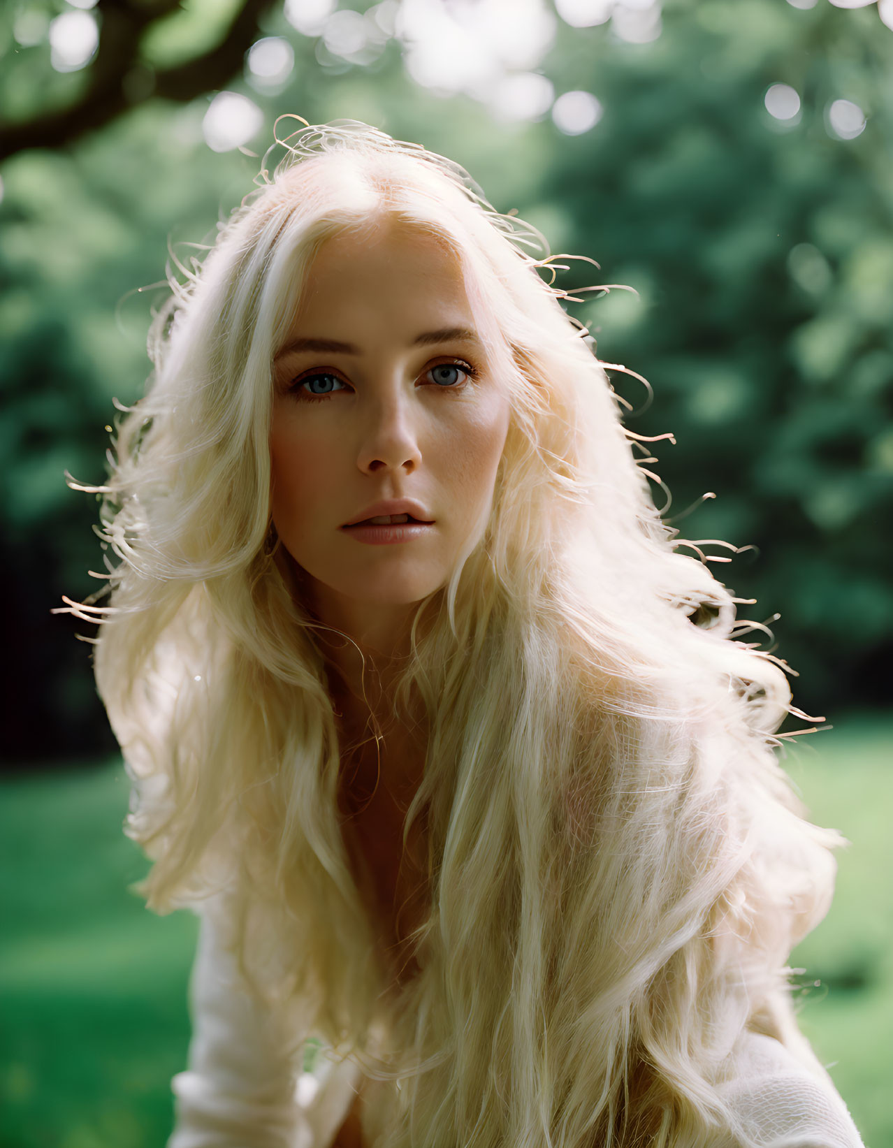 Blonde woman with blue eyes against lush green backdrop