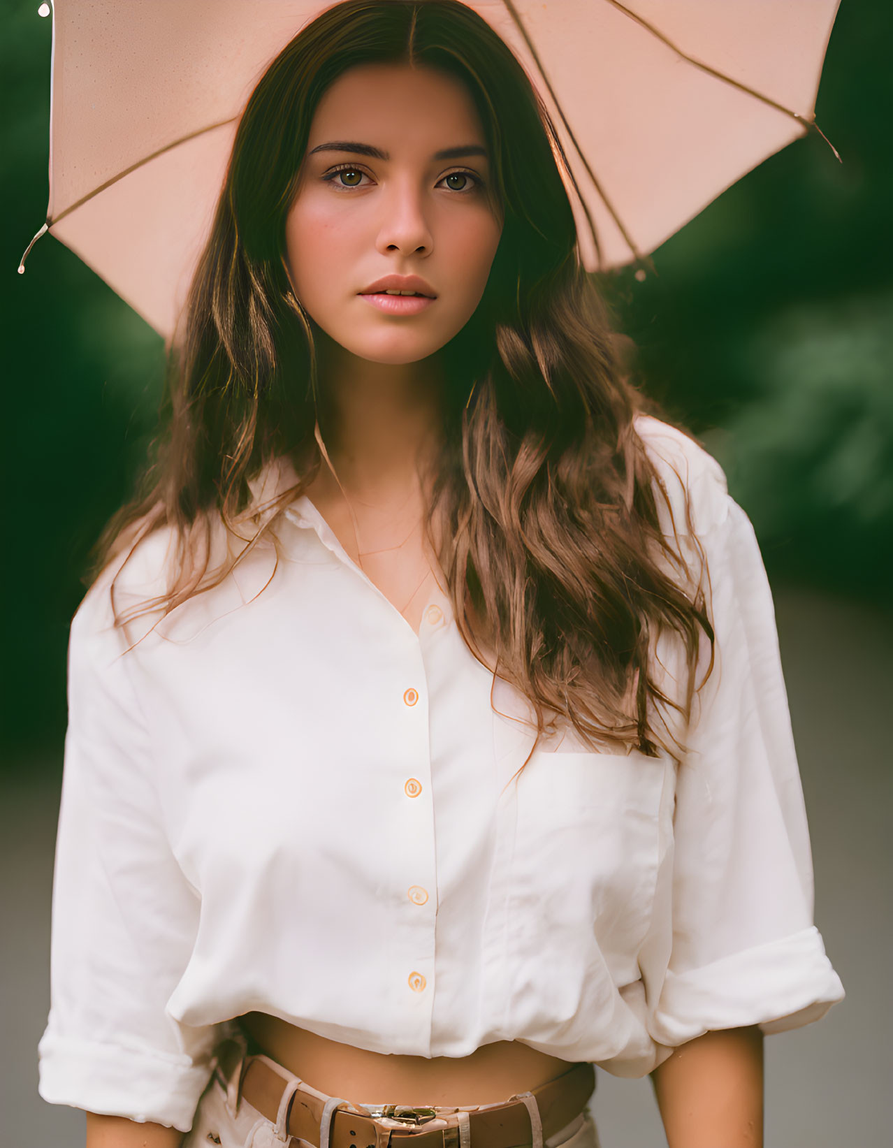 Woman with long wavy hair holding pale umbrella in white blouse and beige skirt.