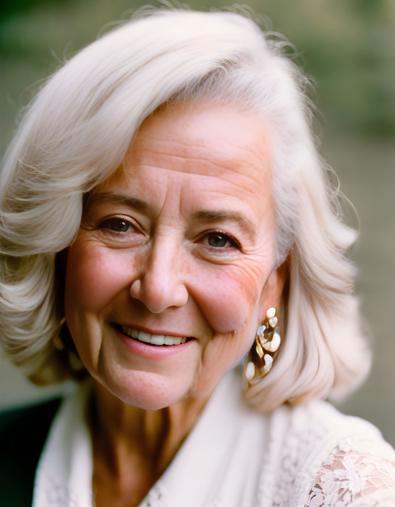 Elderly woman with white hair smiling in white blouse