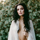 Dark-haired woman in white draped garment against green foliage