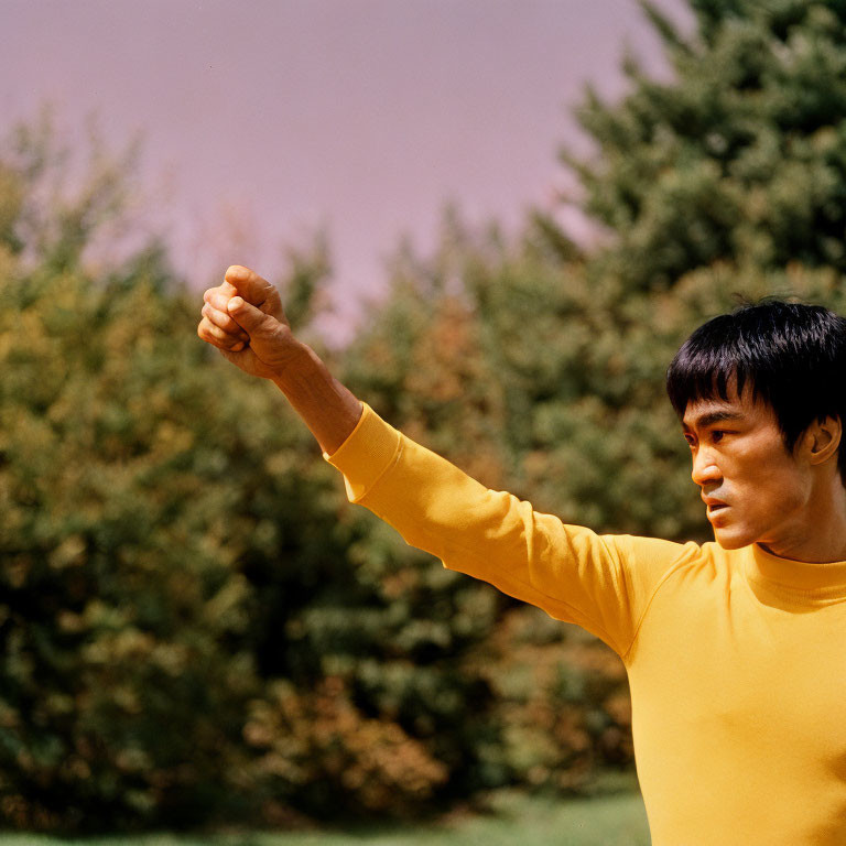 Confident man in yellow shirt practicing martial arts outdoors with trees in background