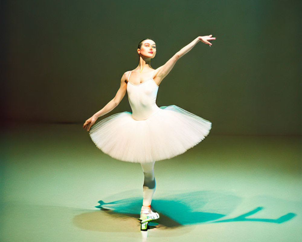 Ballerina in white tutu performs on pointe with extended arm on brightly lit stage