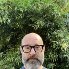 Bald Person with Beard, Glasses, Blue Top, Green Background