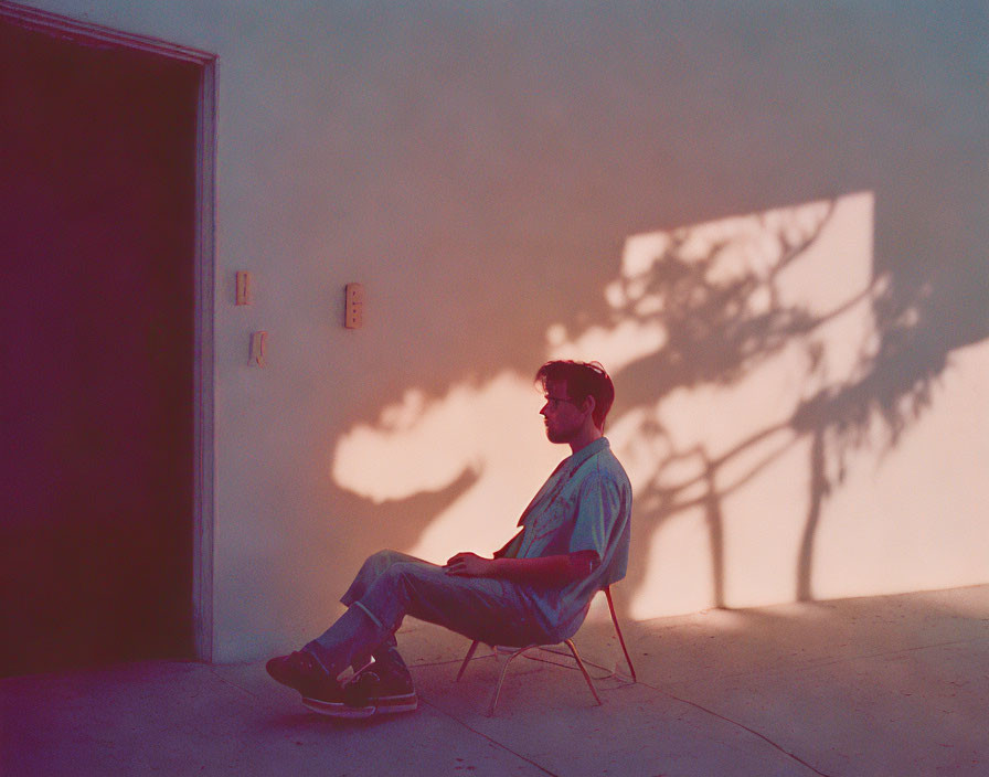 Person sitting on folding chair by door with tree shadows at sunset