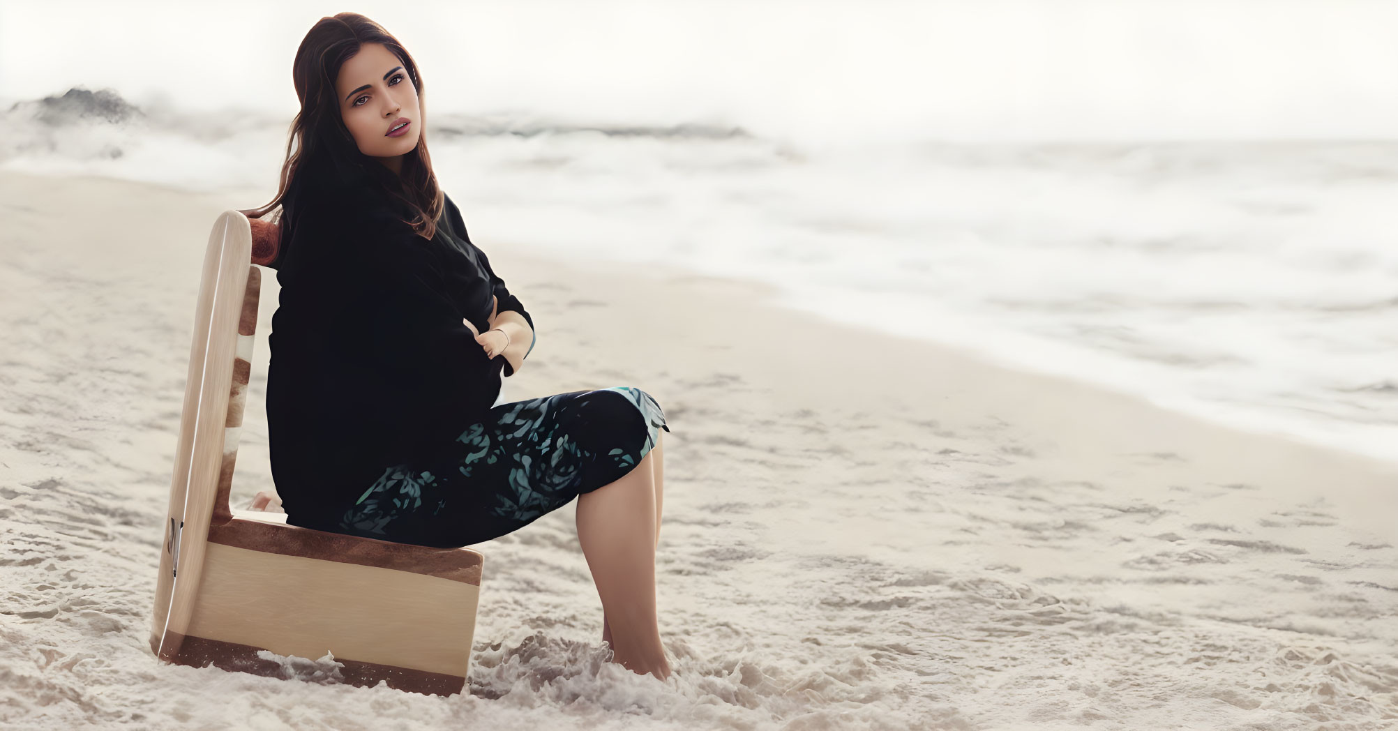 Woman sitting by ocean in black outfit with hair down