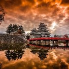 Tranquil cabin by calm lake with ducks, autumn trees, vibrant orange sky