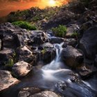 Tranquil creek with moss-covered stones and autumn foliage in sunlight