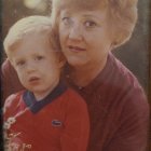 Portrait of young woman and child with blonde curly hair and blue eyes in red attire.