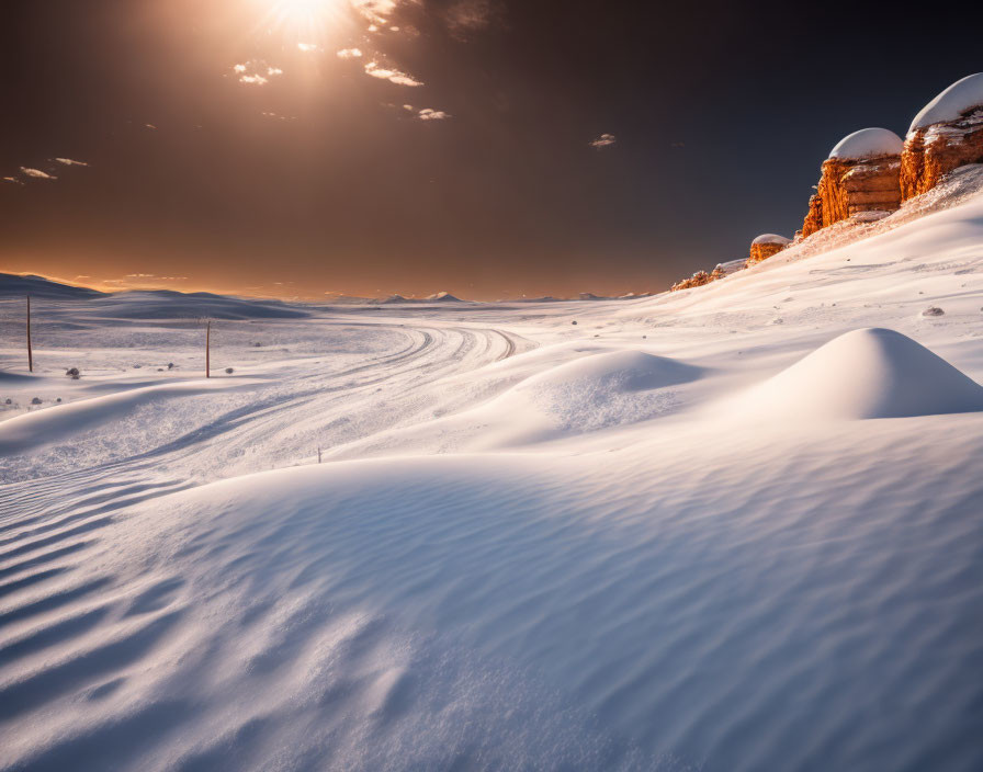 Winter landscape with low sun, long shadows, snow trails, and distant rock formations