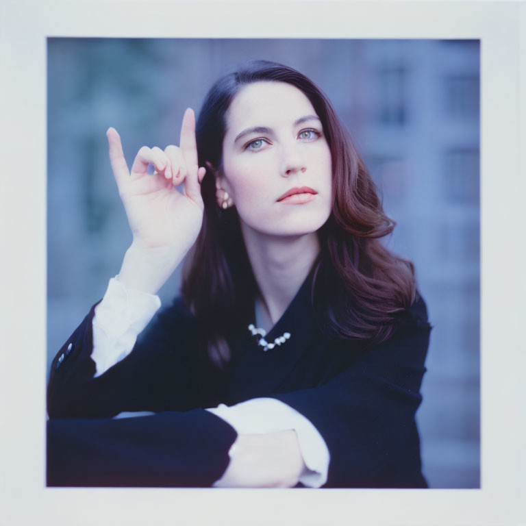 Dark-haired woman in black coat and white blouse, pointing upwards on blue background