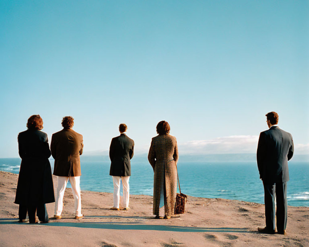 Five people in vintage formal wear on sandy beach by ocean