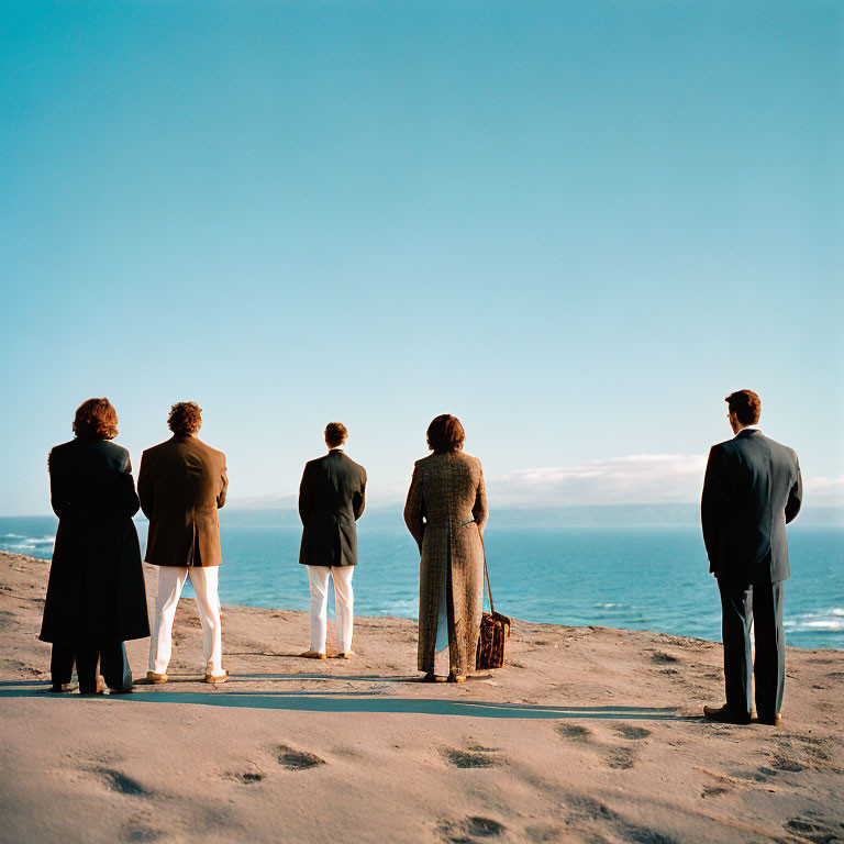 Five people in vintage formal wear on sandy beach by ocean