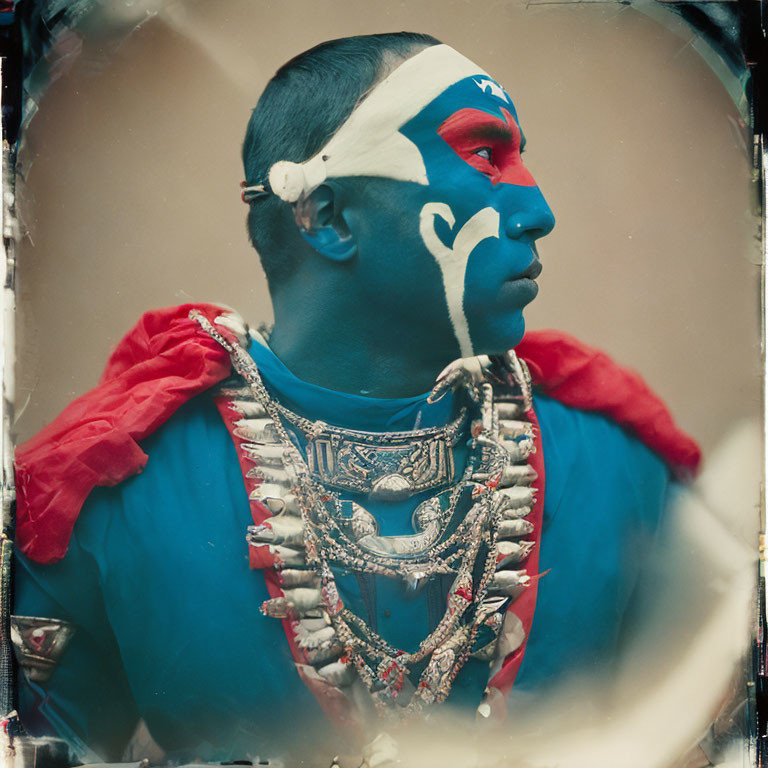 Person in blue and white face paint with beaded necklaces and red cloak gazing sideways