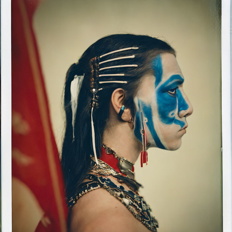 Portrait of person with blue facial paint and feather accessories on muted background