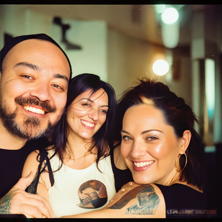 Three Smiling People with Visible Tattoos in Warmly Lit Interior