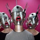 Futuristic androids with metallic headgear and face paint on pink background