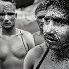 Monochrome image of three men in mud, one with focused intense eyes