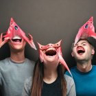 Three people wearing fish masks laughing in front of grey background with confetti