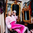 Woman in pink fur outfit applying lipstick at cluttered vanity