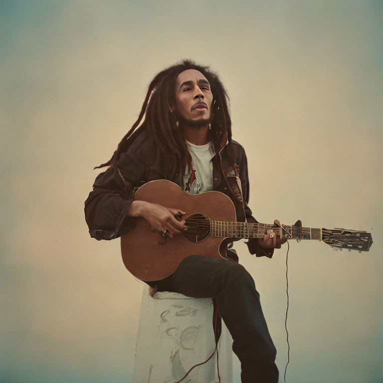 Man playing acoustic guitar with dreadlocks under cloudy sky