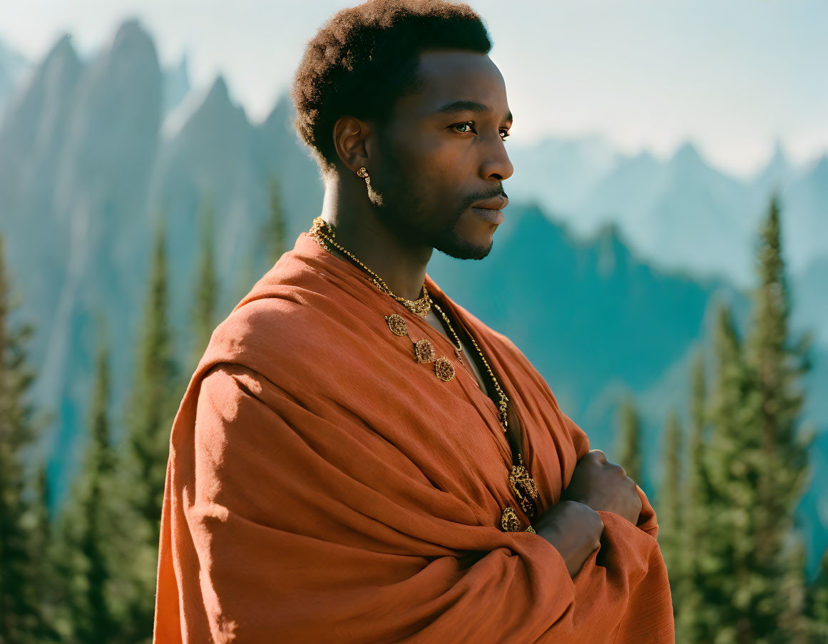 Contemplative man in orange robe with gold jewelry against mountain backdrop