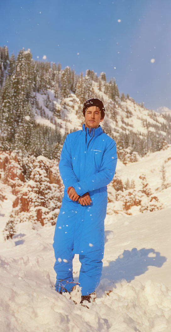 Person in Blue Ski Suit Standing in Snow with Pine Trees and Mountain Background