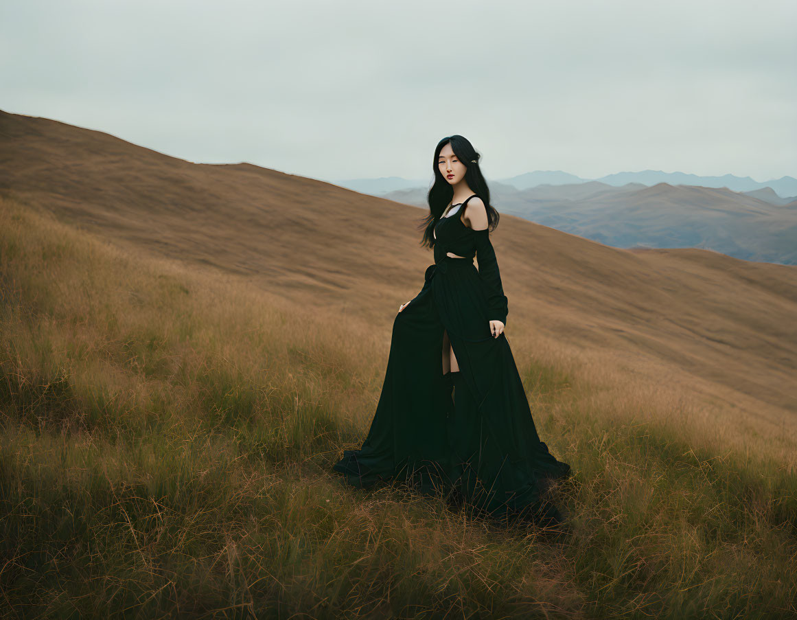Woman in black dress on grassy hill under overcast sky