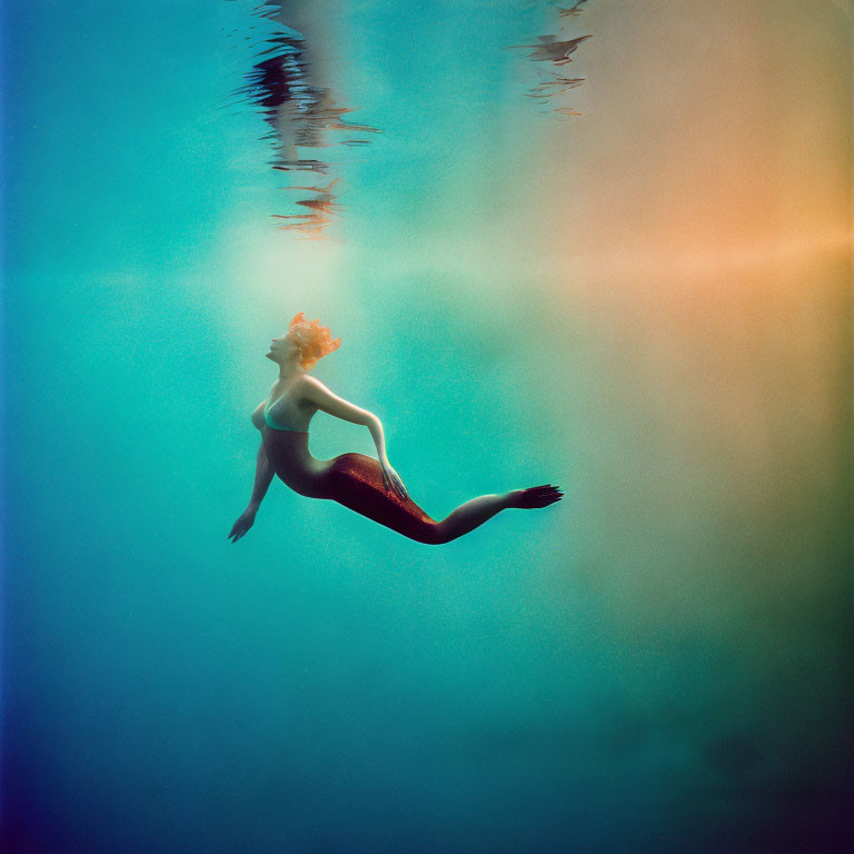 Mermaid-like figure with red tail underwater in surreal lighting