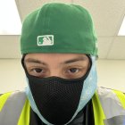 Person with Blue Eyes in Green Beanie, Black Face Mask, Yellow Jacket, and Silver Umbrella