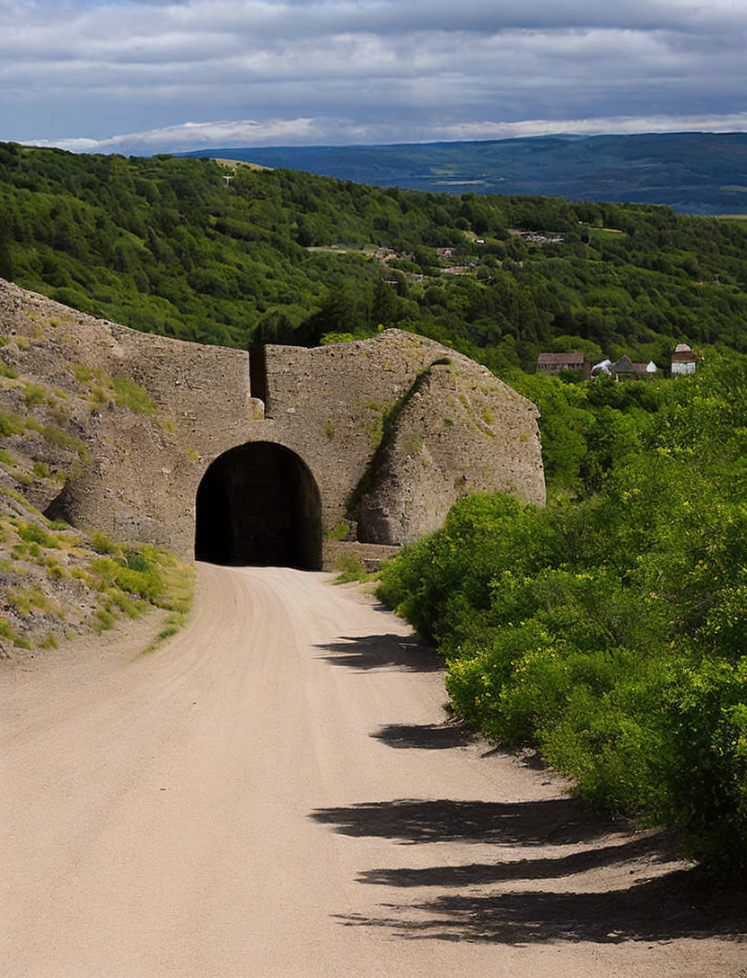 Rustic dirt road to old stone tunnel surrounded by lush greenery